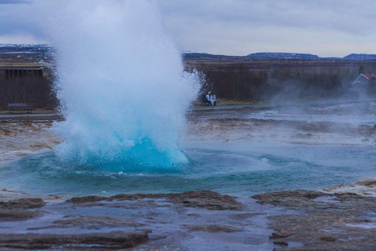 chaudière geothermie avec un geyser entouré de collines sous un ciel nuageux en Islande