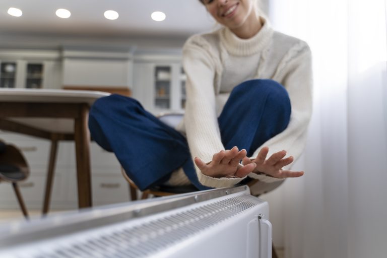 geothermie chauffage maison femme profitant de la chaleur d’un radiateur à la maison