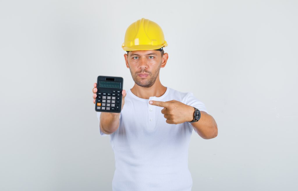 prix géothermie verticale avec un ouvrier en t-shirt blanc et casque pointant une calculatrice sur un chantier