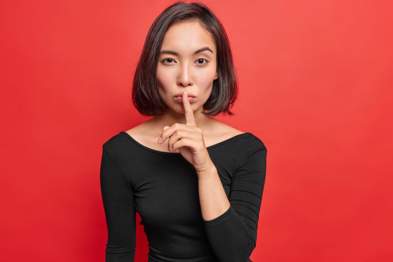 zubadan silence jeune femme asiatique sérieuse fait un geste de silence sur fond rouge vif